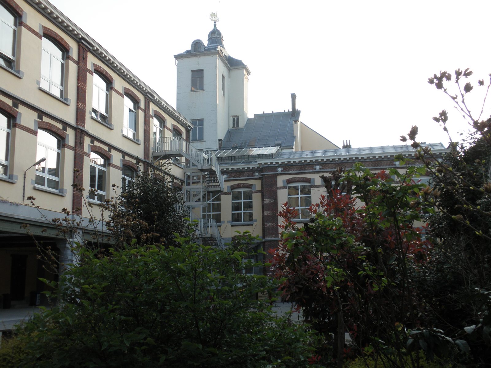 Cour de l’implantation Marché-aux-Grains avec ses façades de brique et de pierre et la tour surmontée d’une girouette en forme de navire